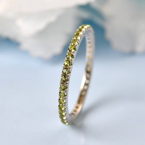 Op de afbeelding: Een delicate eeuwigheidsring met een rij kleine, groene edelstenen gezet in een zilveren band.