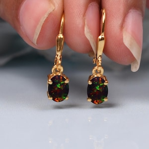 May include: A pair of gold earrings with oval-shaped black and green opal gemstones.