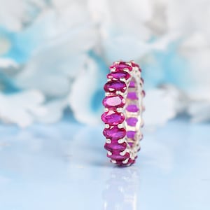 May include: A silver band ring with a row of oval-shaped pink gemstones.