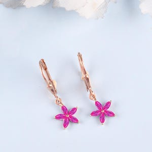 May include: A pair of rose gold leverback earrings, each featuring a dangling flower-shaped charm composed of five vibrant fuchsia pink marquise-cut stones arranged in a star-like pattern, connected to a simple metal hook mechanism.