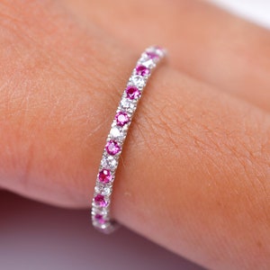 May include: A delicate eternity band with alternating pink and white gemstones. The band is set in a white metal.