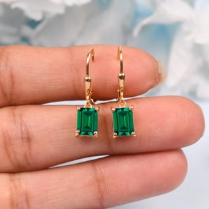 Puede incluir: Pendientes de aro dorados con piedras preciosas cuadradas de color verde esmeralda que cuelgan de la parte inferior.