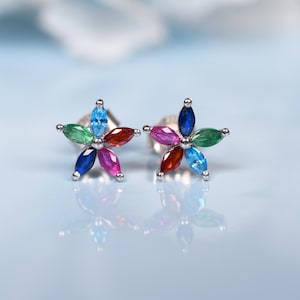 Puede incluir: Un par de pendientes de botón con forma de flor. Cada pendiente presenta seis gemas de talla marquesa en una variedad de colores: azul, verde, rojo, rosa y morado. Los pendientes están engastados en un metal plateado.