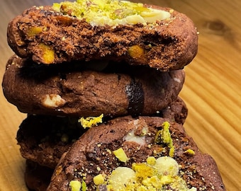 May include: A stack of four chocolate chip cookies topped with white chocolate chips and chopped pistachios. The cookies are on a wooden surface. The text "Kiko Vegan Cookies" is visible at the bottom of the image. The text "@kikovegancookies" is visible on the cookie.