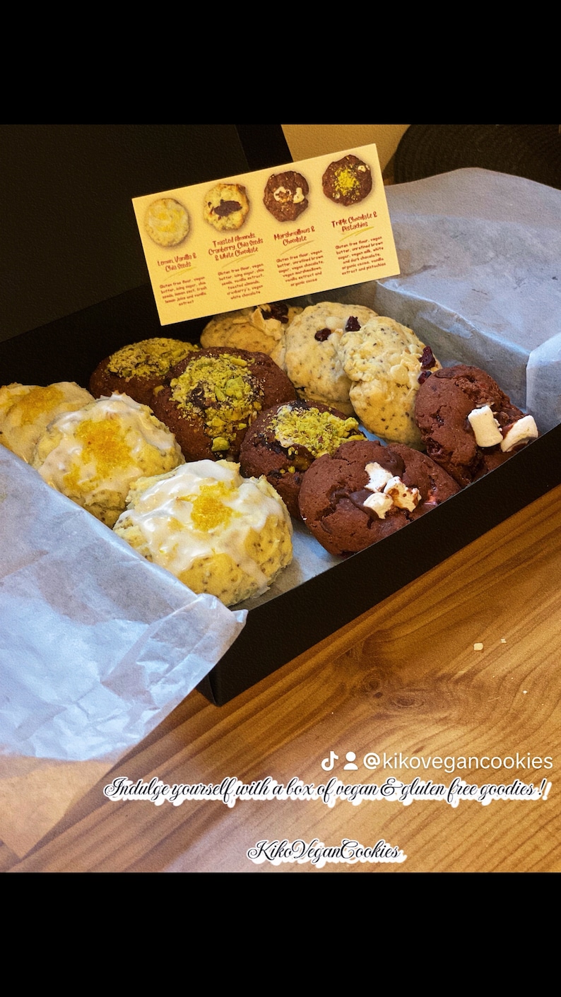 May include: A box of assorted vegan and gluten-free cookies. The cookies are arranged in a black box with white tissue paper. The cookies include lemon vanilla, toasted almond cranberry oat crumble,  marvellous chocolate, and triple chocolate & potato. The box has a sticker that says "Indulge yourself with a box of vegan & gluten free goodies!" and "Kiko Vegan Cookies".
