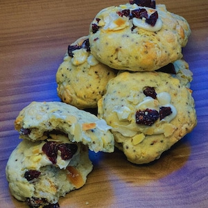 May include: A stack of four vegan cookies with white chocolate chips, cranberries, and a light glaze. The cookies are on a wooden surface. The text "Kiko Vegan Cookies" is visible in the bottom right corner of the image.