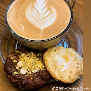 May include: A cup of coffee with latte art, a chocolate cookie with pistachio topping, and a lemon cookie with white icing. The text on the image reads "#Coffee Break Kiko Vegan Smile @kikovegancookies".