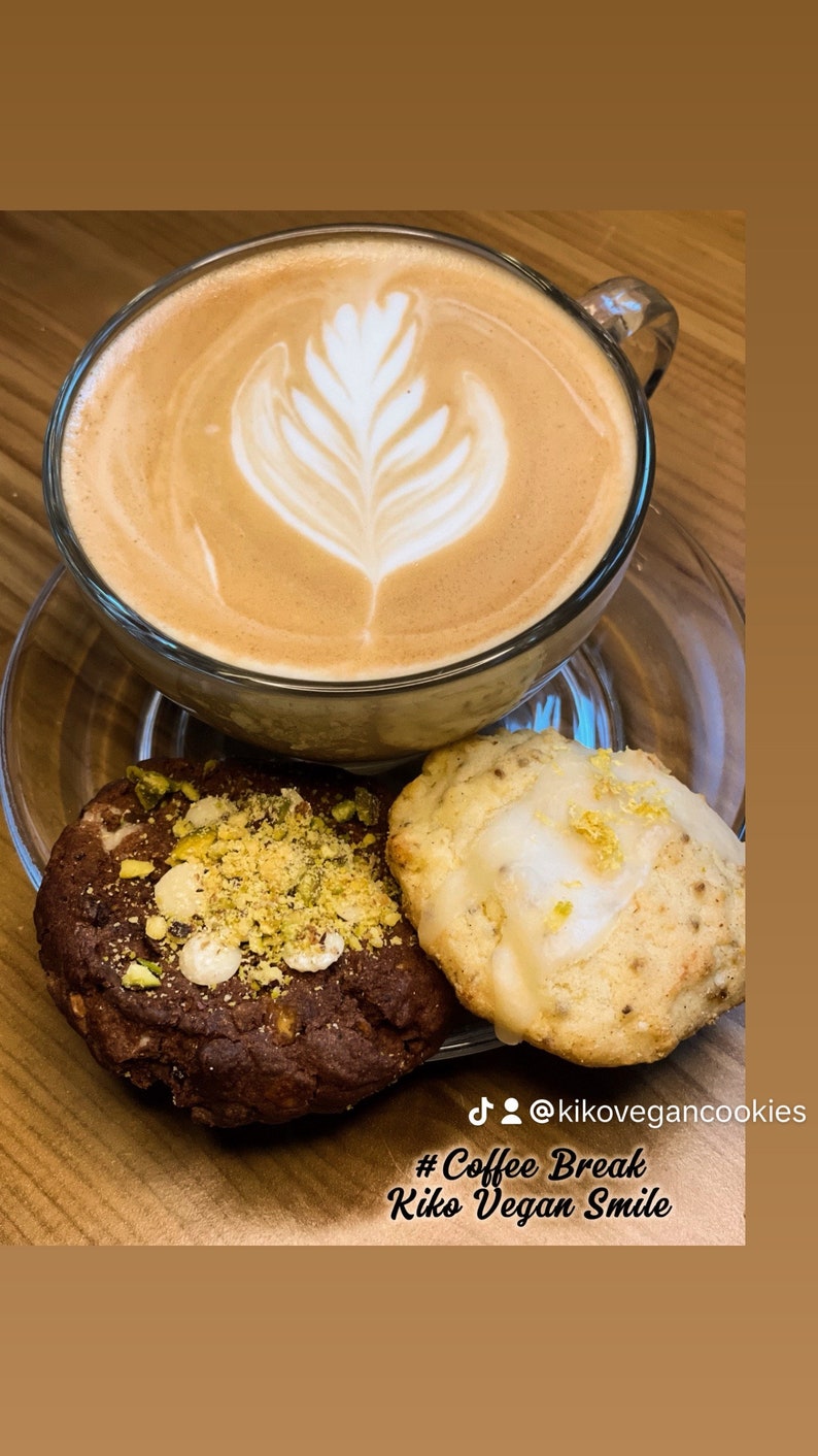 May include: A cup of coffee with latte art, a chocolate cookie with pistachio topping, and a lemon cookie with white icing. The text on the image reads "#Coffee Break Kiko Vegan Smile @kikovegancookies".