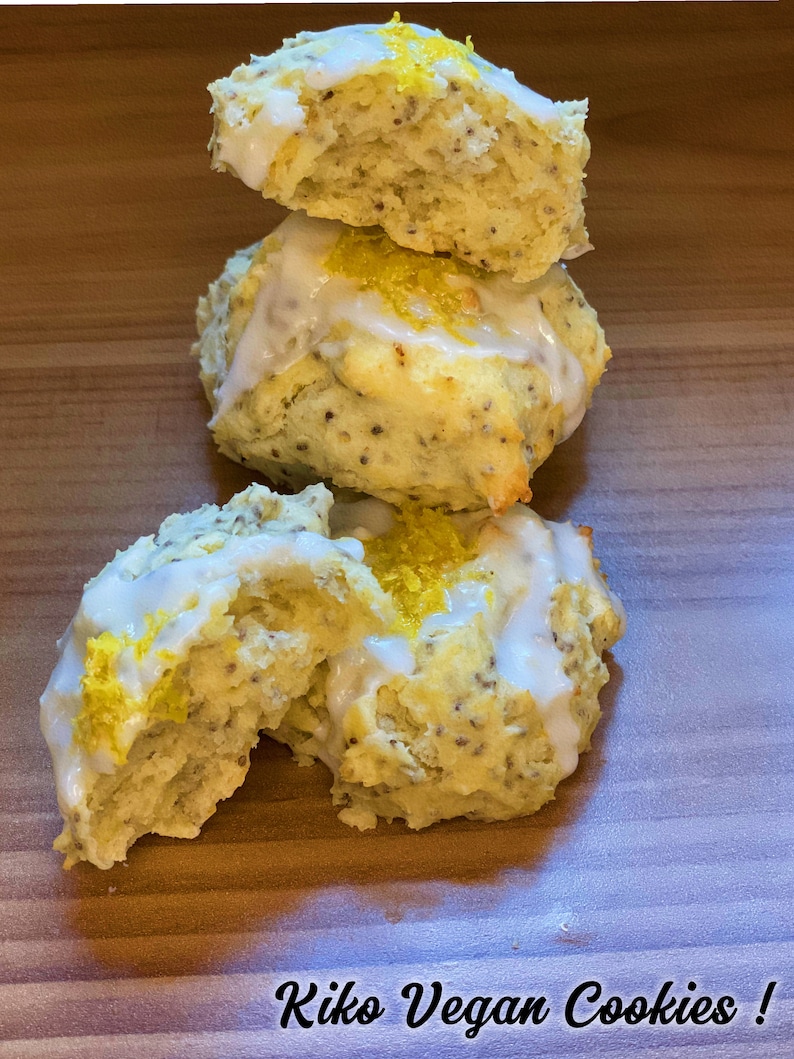 May include: Three vegan lemon poppyseed cookies with a white glaze and lemon zest on top. The cookies are stacked on top of each other on a wooden surface. The text "Kiko Vegan Cookies!" is written below the cookies.