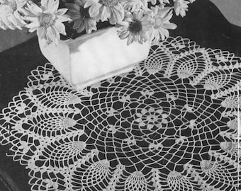 Puede incluir: Un tapete blanco tejido a crochet con un diseño calado detallado, con un motivo floral central y bordes festoneados. Un jarrón rectangular blanco contiene un ramo de margaritas blancas. El arreglo está sobre una superficie oscura.