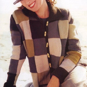May include: A patchwork cardigan in a variety of colours, with wooden buttons. The sweater has a checkerboard design in shades of grey, beige, and olive green. The person in the image is wearing a grey hat.
