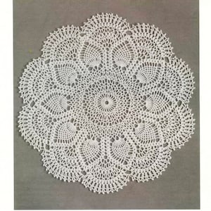 May include: A white, circular, crocheted doily with a detailed, openwork design. The doily features a central circular pattern surrounded by repeating fan-shaped motifs, creating a delicate and intricate texture. The overall diameter is approximately 12 inches.