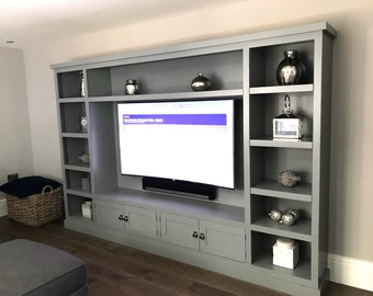 May include: A grey entertainment unit with a large flat screen TV, shelves, and cupboards. The shelves are decorated with decorative items, including vases, lanterns, and ornaments.