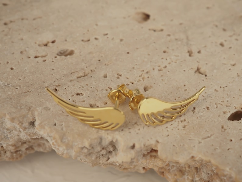 Puede incluir: Un par de pendientes de color dorado con forma de alas de &aacute;ngel. Las alas son delicadas y tienen una forma ligeramente curvada.