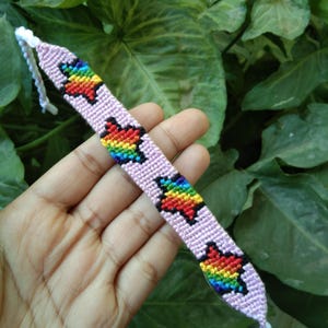 May include: A pink friendship bracelet with rainbow coloured stars woven into the design.