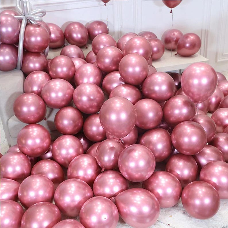 May include: A large group of rose gold metallic balloons. The balloons are arranged in a pile and are all inflated.