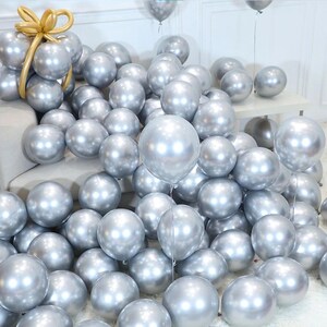 May include: A large group of silver chrome balloons, some are tied together and others are loose. The balloons are arranged in a cascading pattern on a white surface.