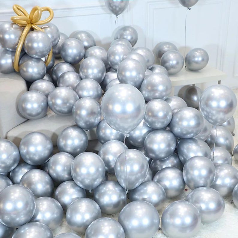 May include: A large group of silver chrome balloons, some are tied together and others are loose. The balloons are arranged in a cascading pattern on a white surface.