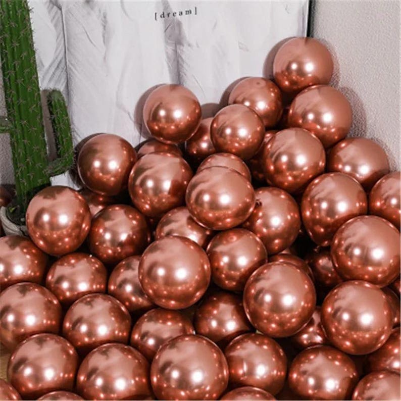 May include: A large pile of rose gold metallic balloons. The balloons are shiny and reflect light.