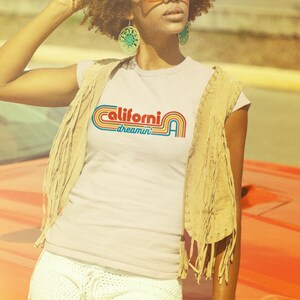 Op de afbeelding: Een wit T-shirt met een retro-grafische afbeelding met de tekst "California dreamin'" in regenboogkleuren.
