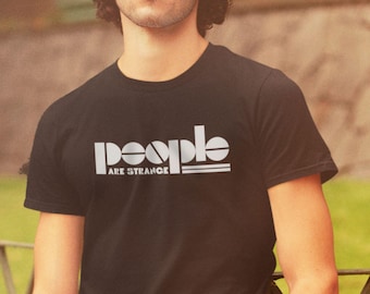 May include: Black t-shirt with the white text "people" above "ARE STRANGE" in a bold, sans-serif font. The shirt is a classic crew neck style.