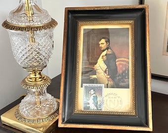 Op de afbeelding: Geraamde portret van een man in militair uniform, met een postzegel van een man in militair uniform. De lijst is zwart met een gouden binnenrand. Het portret is van een man met een strenge uitdrukking.