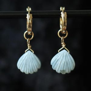 Peut inclure: Une paire de boucles d'oreilles créoles en or avec un charme coquillage bleu clair suspendu à chaque créole.