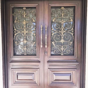 Puede incluir: Un par de puertas de madera marrón oscuro con elementos decorativos de metal dorado y paneles de vidrio. Las puertas presentan adornos de volutas y dos manijas verticales. Los paneles inferiores tienen detalles rectangulares empotrados.