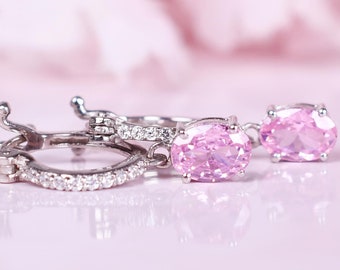 May include: A pair of silver hoop earrings with pink oval-shaped gemstones. The earrings are set with small clear stones around the edge of the hoops.