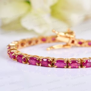 Op de afbeelding: Een gouden armband met een rij ovale roze edelstenen. De armband heeft een sluiting.