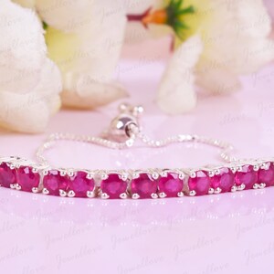 May include: A silver bracelet featuring a row of red gemstones. The bracelet has an adjustable sliding clasp.