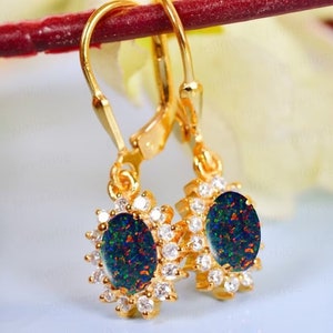 May include: A pair of gold dangle earrings with a black opal gemstone surrounded by a halo of clear cubic zirconia stones.