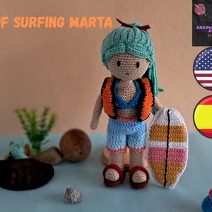 Könnte beinhalten: Gehäkelte Puppe namens Marta, bekleidet mit einem Surf-Outfit, hält ein Surfbrett. Die Puppe hat ein türkisfarbenes Kopftuch, eine orangefarbene und schwarze Weste, blaue Shorts und rote Sandalen. Das Surfbrett ist weiß, orange, rosa und gelb. Der Text auf dem Bild lautet "PDF SURFING MARTA".