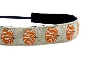 May include: A beige headband with a black elastic band and a repeating pattern of orange pumpkins with white outlines.