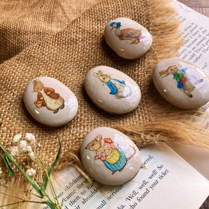 Puede incluir: Cinco piedras pintadas con personajes del libro infantil 'El cuento de Peter Rabbit'. Las piedras están pintadas con Peter Rabbit, Benjamin Bunny, Jemima Puddle-Duck, Mrs. Tiggy-Winkle y Mr. McGregor.