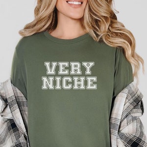 Puede incluir: Una camiseta verde de manga larga con el texto "VERY NICHE" en letras blancas con una fuente de estilo universitario.