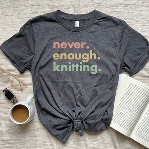 May include: A dark grey t-shirt with the text "never. enough. knitting." in a rainbow colour scheme.