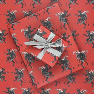 May include: Red wrapping paper with a repeating pattern of black devil figures. A wrapped gift box with a silver ribbon sits on top of the paper. The gift box and paper are a matching red color.