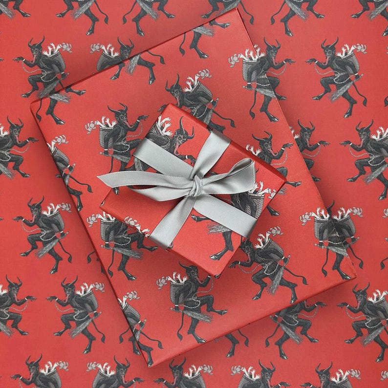 May include: Red wrapping paper with a repeating pattern of black devil figures. A wrapped gift box with a silver ribbon sits on top of the paper. The gift box and paper are a matching red color.