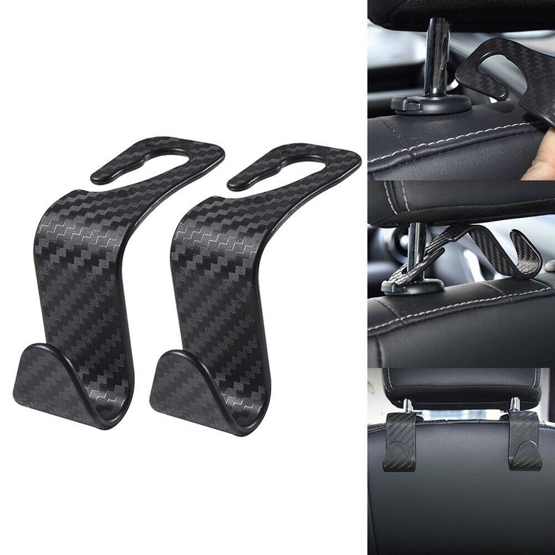 May include: Two black car seat headrest hooks with a carbon fiber pattern. The hooks are designed to hang bags, coats, or other items on the back of a car seat.