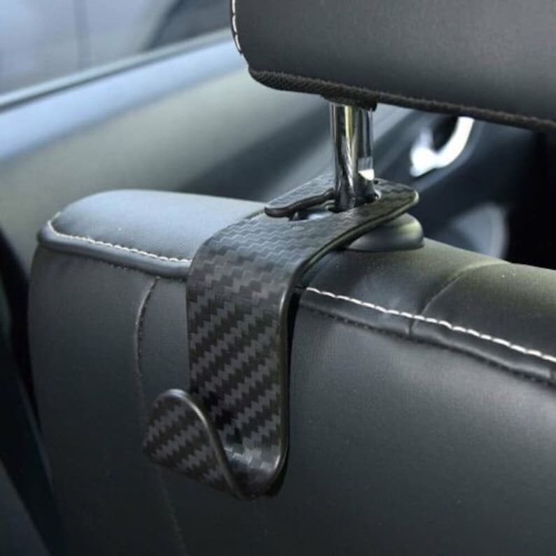 May include: Black car seat hook with a carbon fiber pattern. The hook is designed to hang on the back of a car seat.
