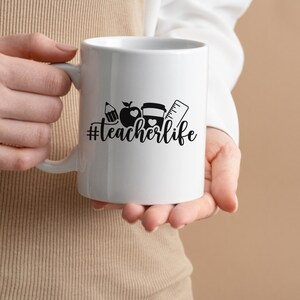 May include: White ceramic mug with a black design of a pencil, apple, and ruler with the text "#teacherlife" on it.