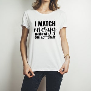 May include: White t-shirt with black text that reads "I match energy so how we gon' act today?"
