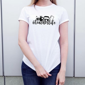 May include: White t-shirt with a black graphic of school supplies and the text "#teacherlife"
