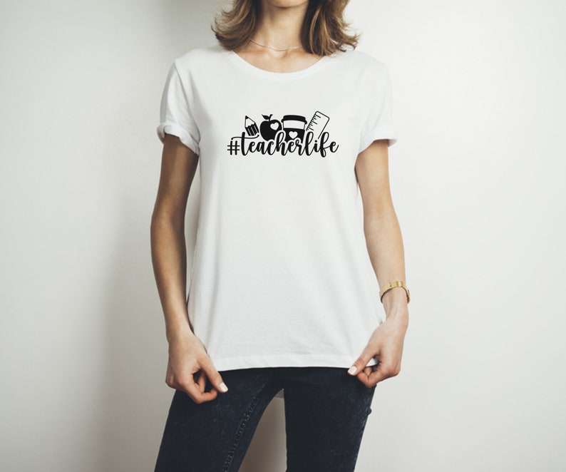 May include: White t-shirt with a black graphic of a pencil, apple, book, and ruler with the text "#teacherlife" printed on the front.