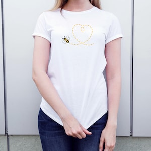 May include: White t-shirt with a yellow heart design and a small bee flying towards it.