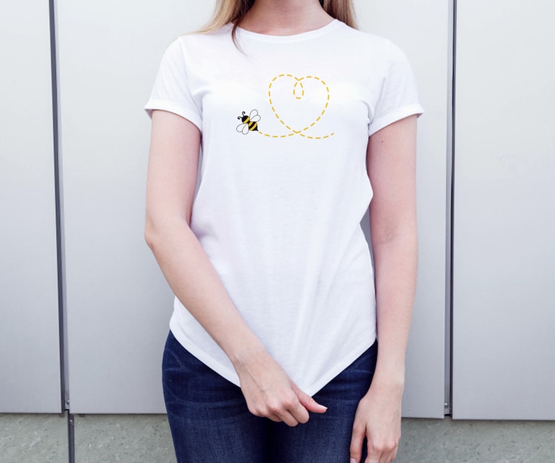 May include: White t-shirt with a yellow heart design and a small bee flying towards it.