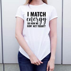 May include: White t-shirt with black text that reads "I match energy so how we gon' act today?"