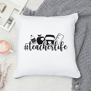 May include: White throw pillow with black text and graphics. The text reads "#teacherlife". The graphics include an apple, a pencil, a coffee cup, and a ruler.