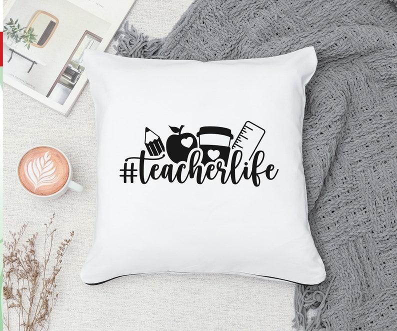 May include: White throw pillow with black text and graphics. The text reads "#teacherlife". The graphics include an apple, a pencil, a coffee cup, and a ruler.